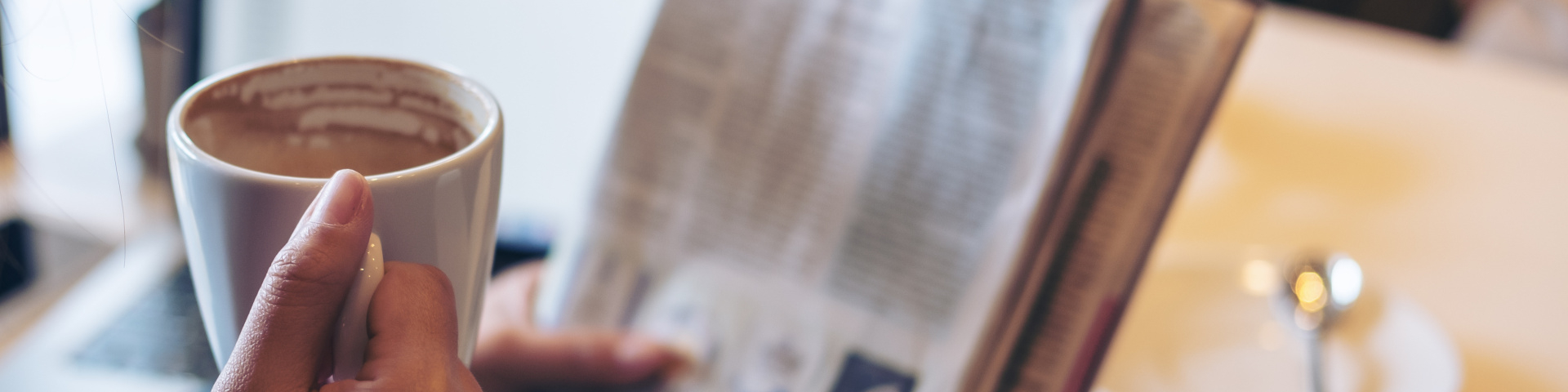 Eine Person liest Zeitung und hält dabei eine Tasse mit einem Heißgetränk.