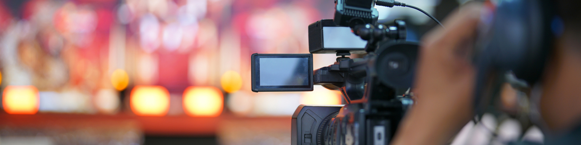 Eine Person filmt mit einer professionellen Videokamera eine Veranstaltung auf einer Bühne.