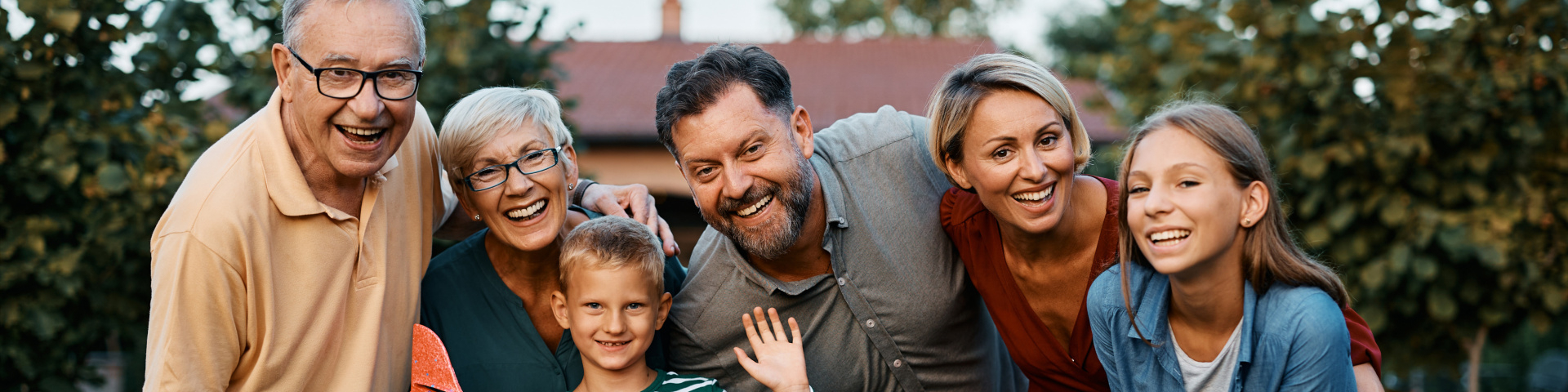 Drei Generationen einer Familie stehen gemeinsam im Garten; ein Junge hält ein Spielzeugflugzeug.